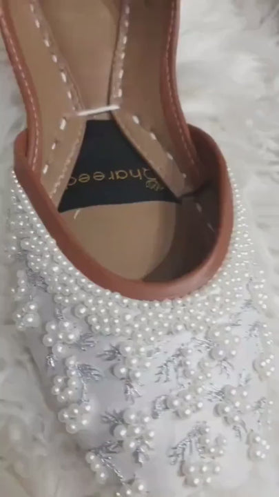 Ivory pearl bridal flats with silver floral embroidery showcased on a white fur rug.