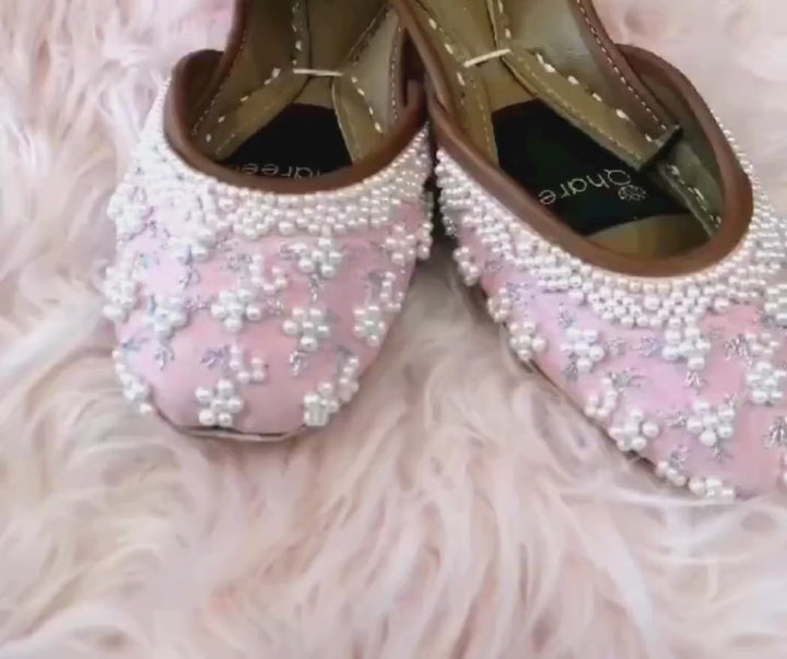 Blush pink pearl bridal flats with silver floral embroidery displayed on a soft pink fur rug, showcasing the handcrafted wedding jutti design.