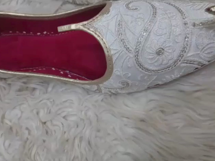 Men’s white embroidered wedding juttis with gold pointed toe caps, gold trim and red lining, shown close up as traditional groom mojari shoes.