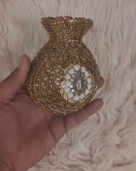 Hand rotating a round gold embellished bridal clutch to show its geometric detailing, white floral accent, sides and back.